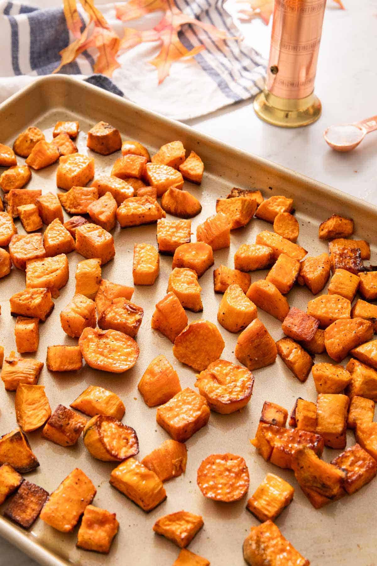 A sheet pan of roasted sweet potatoes with a pepper grinder in the back and some salt.