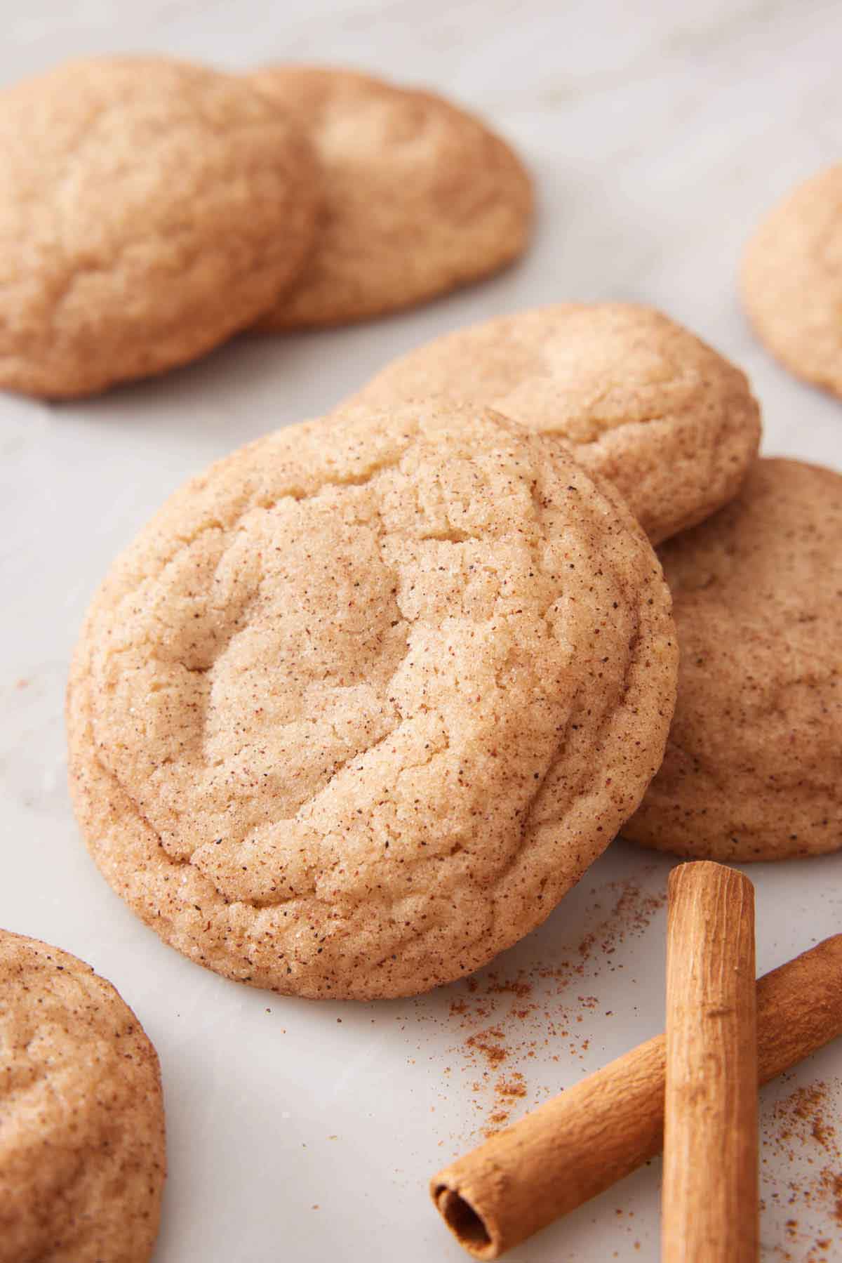 Snickerdoodle cookies in a small grouping with some cinnamon sticks and ground cinnamon scattered nearby.
