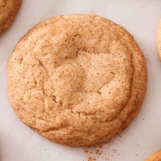 Overhead view of a snickerdoodle cookie with some more off to the side with cinnamon sticks and ground cinnamon.