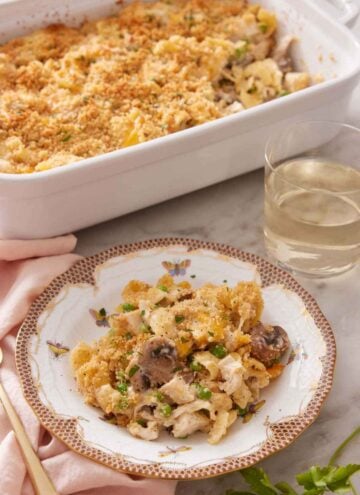 A plate with a serving of turkey casserole with a glass of wine and baking dish behind it.