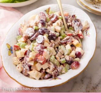 Pinterest graphic of a platter of Waldorf salad with a serving spoon tucked in with lettuce and plates in the background.