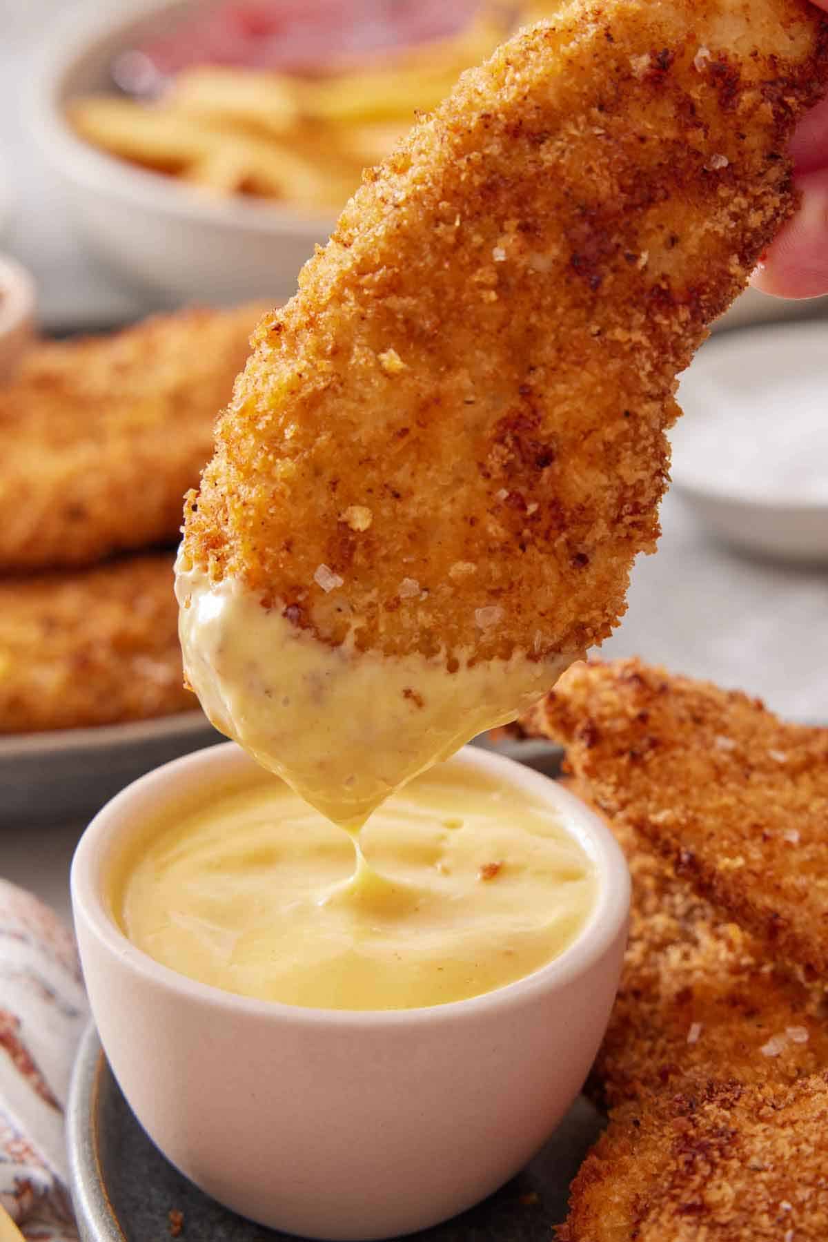 A piece of air fryer chicken tender dipped into mustard.