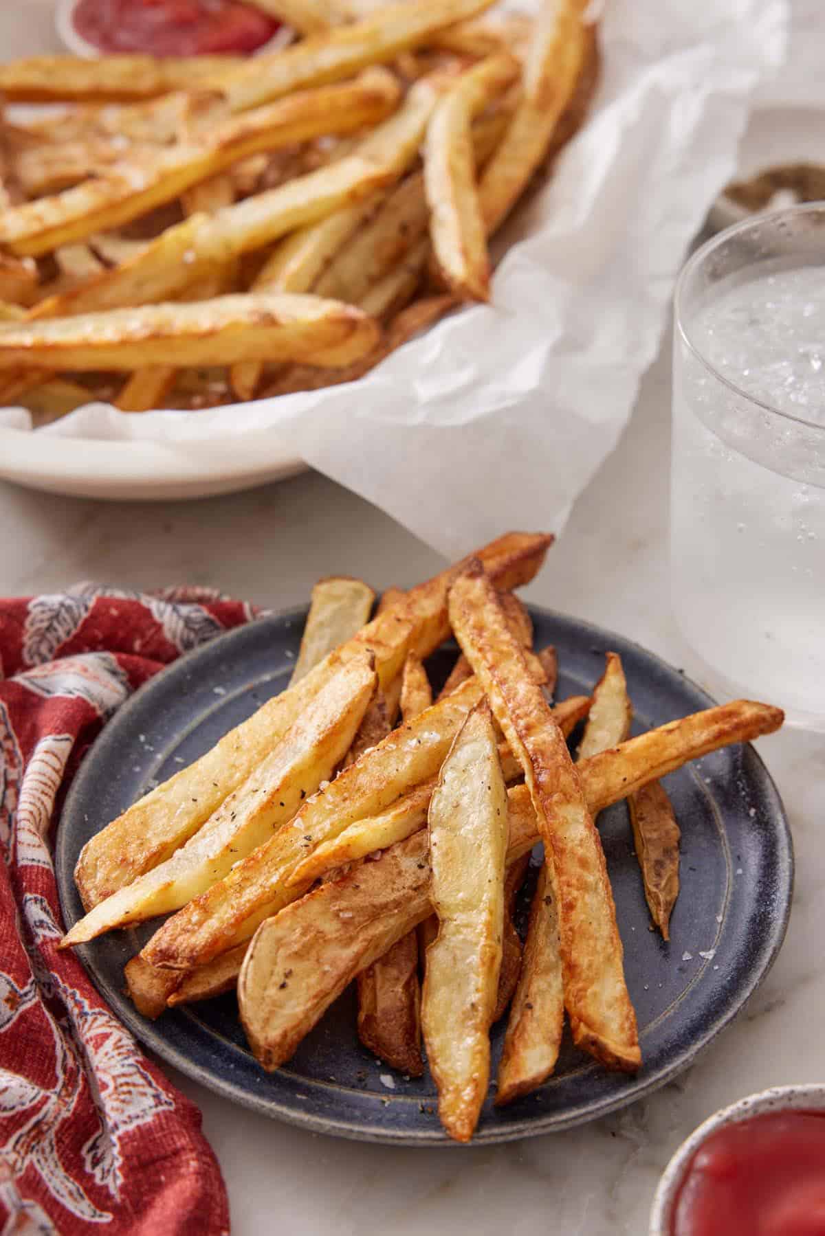 A plate with air fryer french fries with a drink and more fries in the background.
