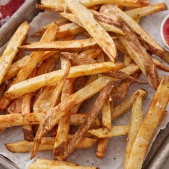 Overhead view of air fryer french fries on a parchment lined sheet pan with ketchup on the side.