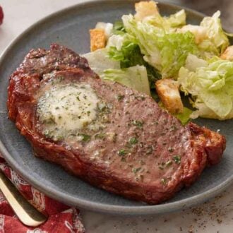 A plate with an air fryer steak and salad with croutons on the side.