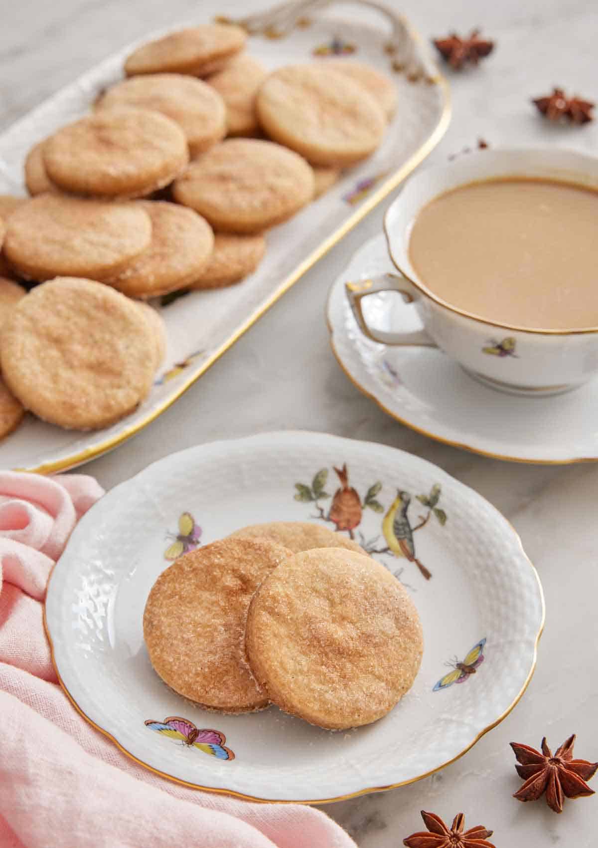 A plate with three biscochitos with a drink in the background with a platter of more cookies.