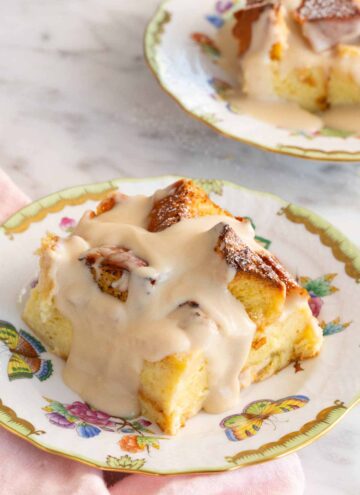 A plate with a serving of bread pudding with a second one in the background, slightly out of frame.