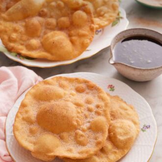Pinterest graphic of a plate with two pieces of bunuelos with more on a platter in the background along with the piloncillo syrup.