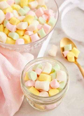 A mason jar with butter mints with a spoonful beside it and a bowl full in the background.