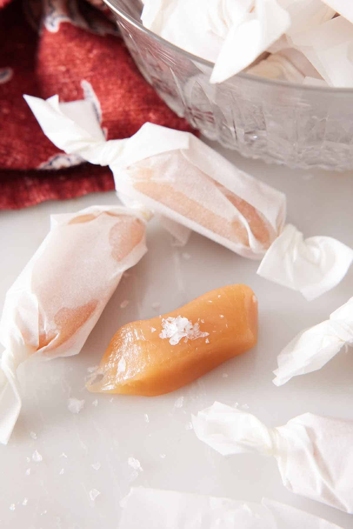 Three homemade caramels with two of them wrapped in paper.