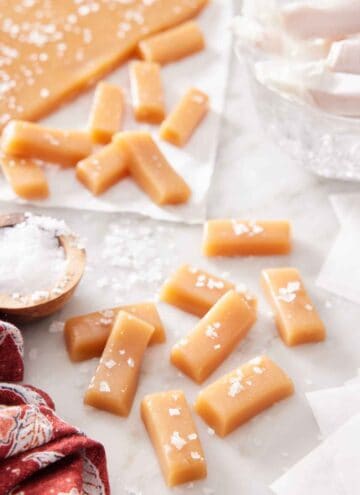 Multiple caramel candies with additional in the background, topped with sea salt.