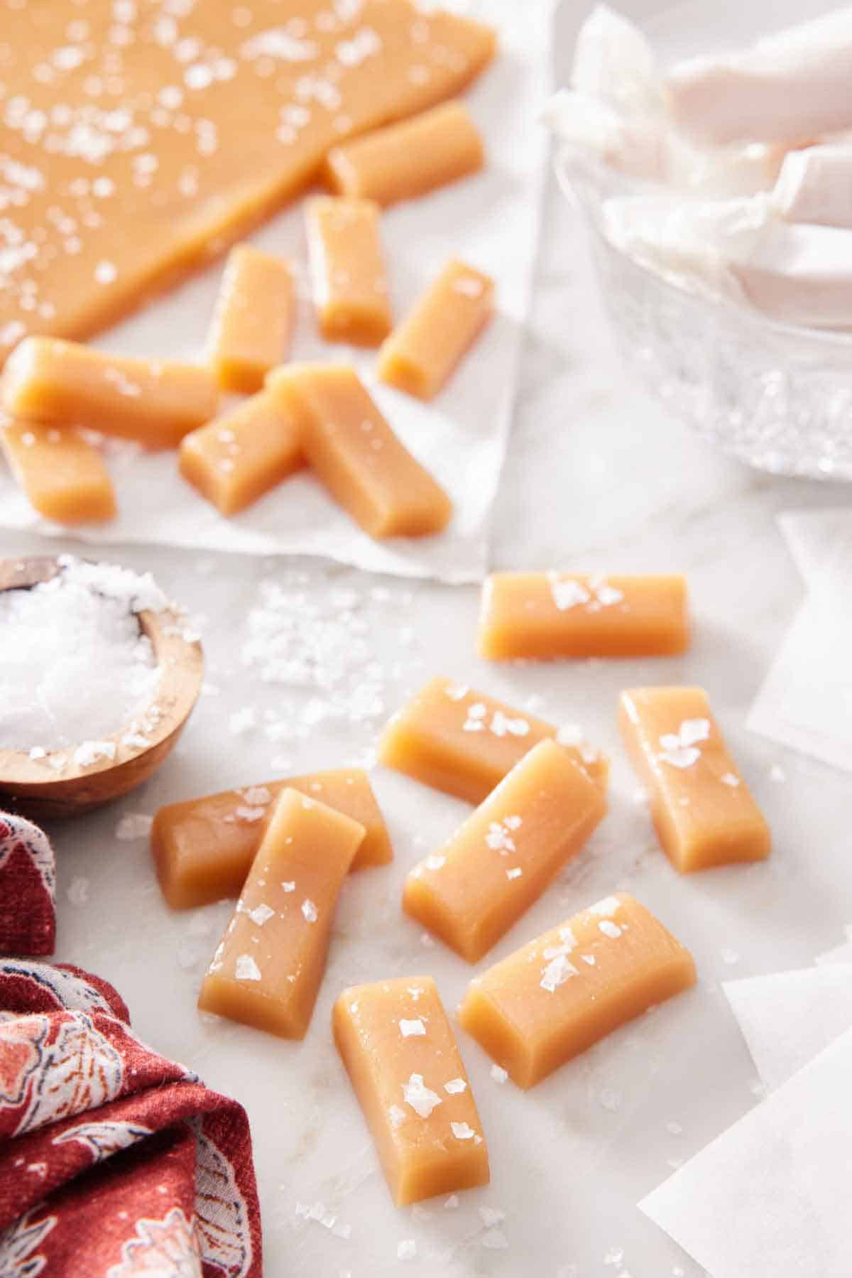 Multiple caramel candies with additional in the background, topped with sea salt.