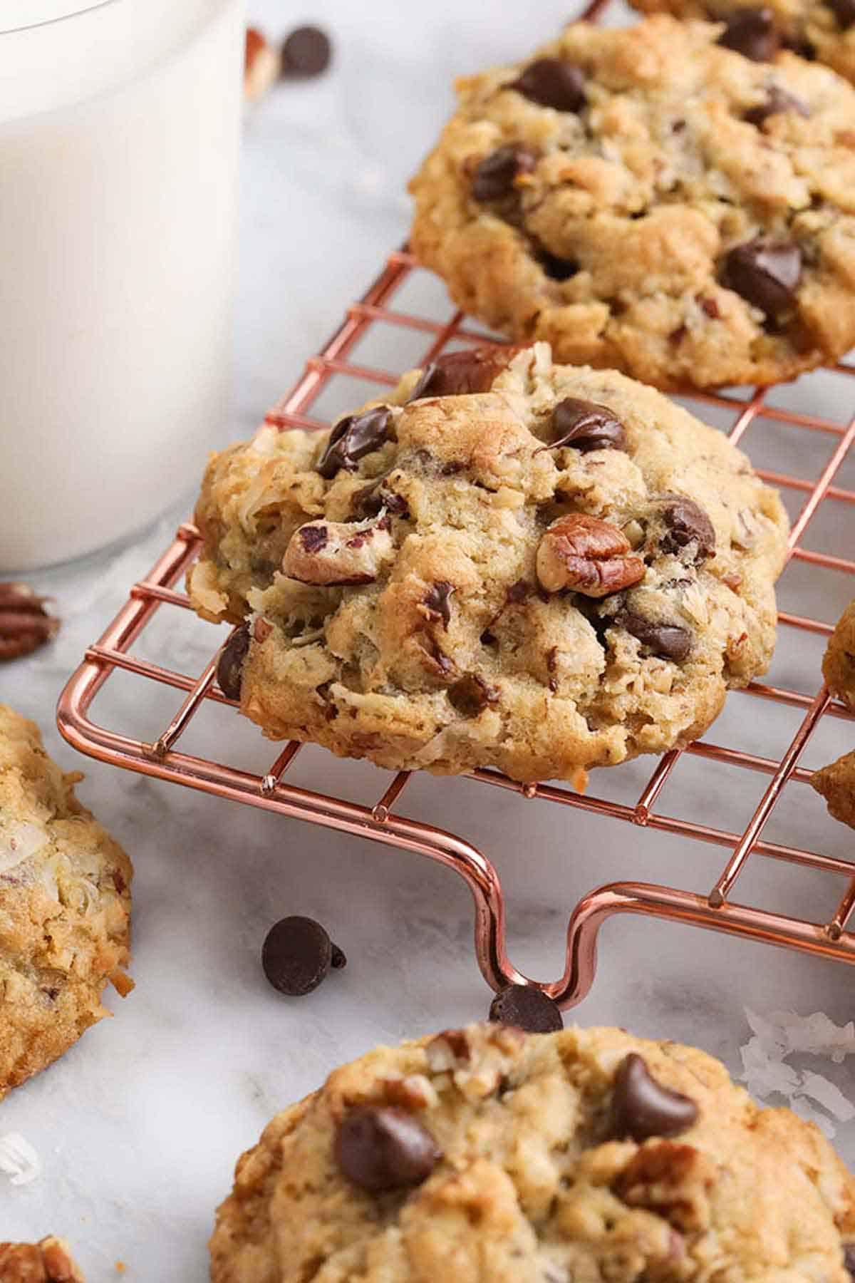 Cowboy cookies on a wire cooling rack with a glass of milk beside it.