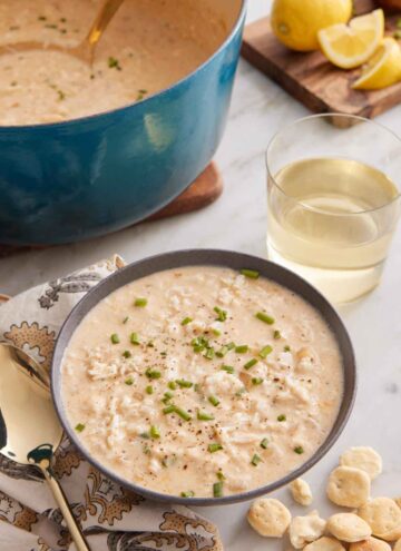 A bowl of crab soup with a drink and pot with the rest of the soup in the background.