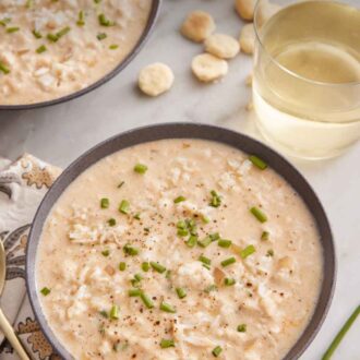 Pinterest graphic of a bowl of crab soup with a drink, bowl of crackers, and additional bowl of soup in the background.