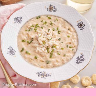 Pinterest graphic of a bowl of crab soup topped with chives with a drink in the background.