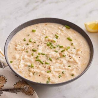 A bowl of crab soup topped with chives with lemon wedges beside it.