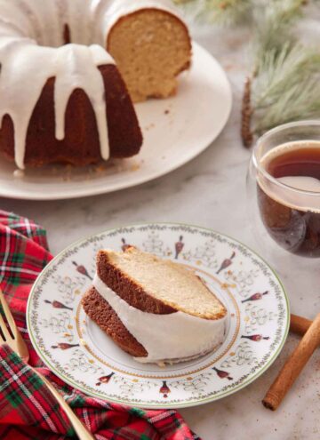 A plate with a slice of eggnog cake with the rest of the cake in the background.