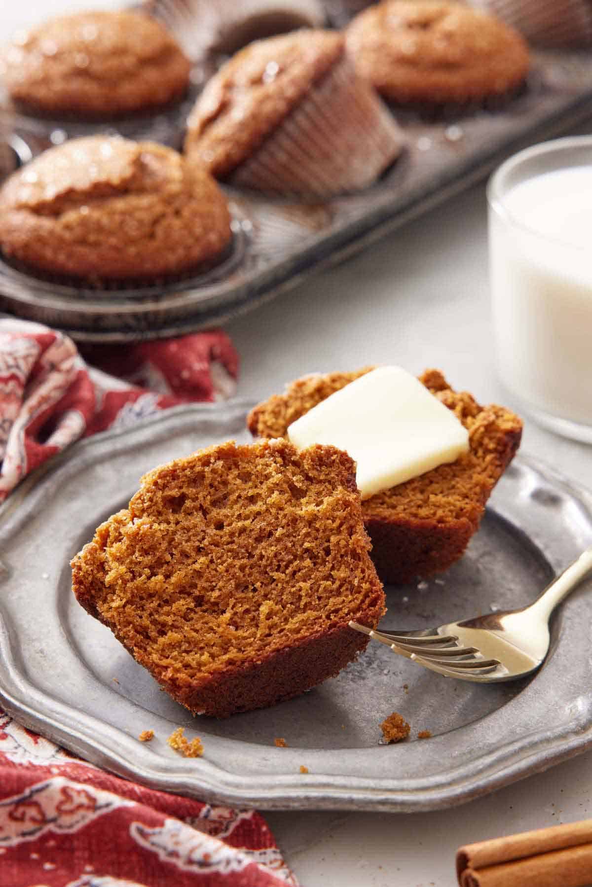 A plate with a gingerbread muffins cut in half with some butter on one side.
