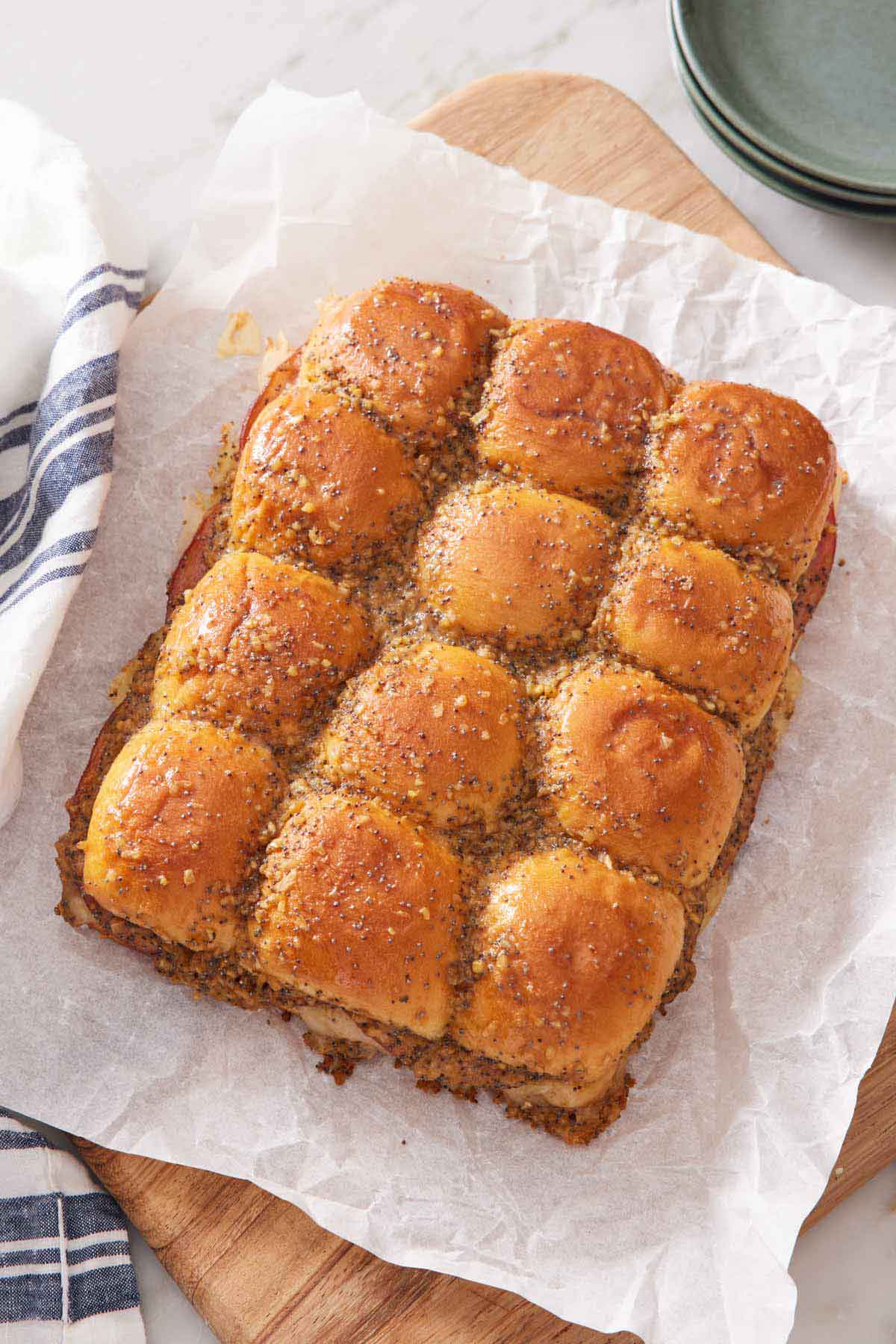 Overhead view of ham and cheese sliders before being sliced on a parchment lined serving board.