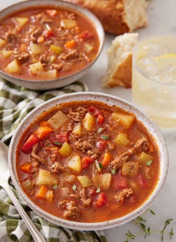 Two bowls of hamburger soup, one in front, with a drink in the background.