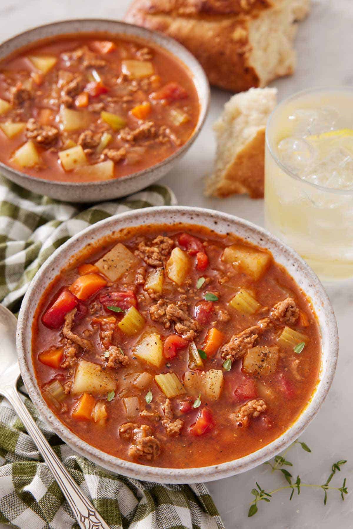 Two bowls of hamburger soup, one in front, with a drink in the background.