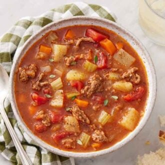 Overhead view of a bowl of hamburger soup with a spoon and drink beside it.