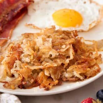 A close view of hash browns on a plate with bacon and a fried egg. Berries in the front.