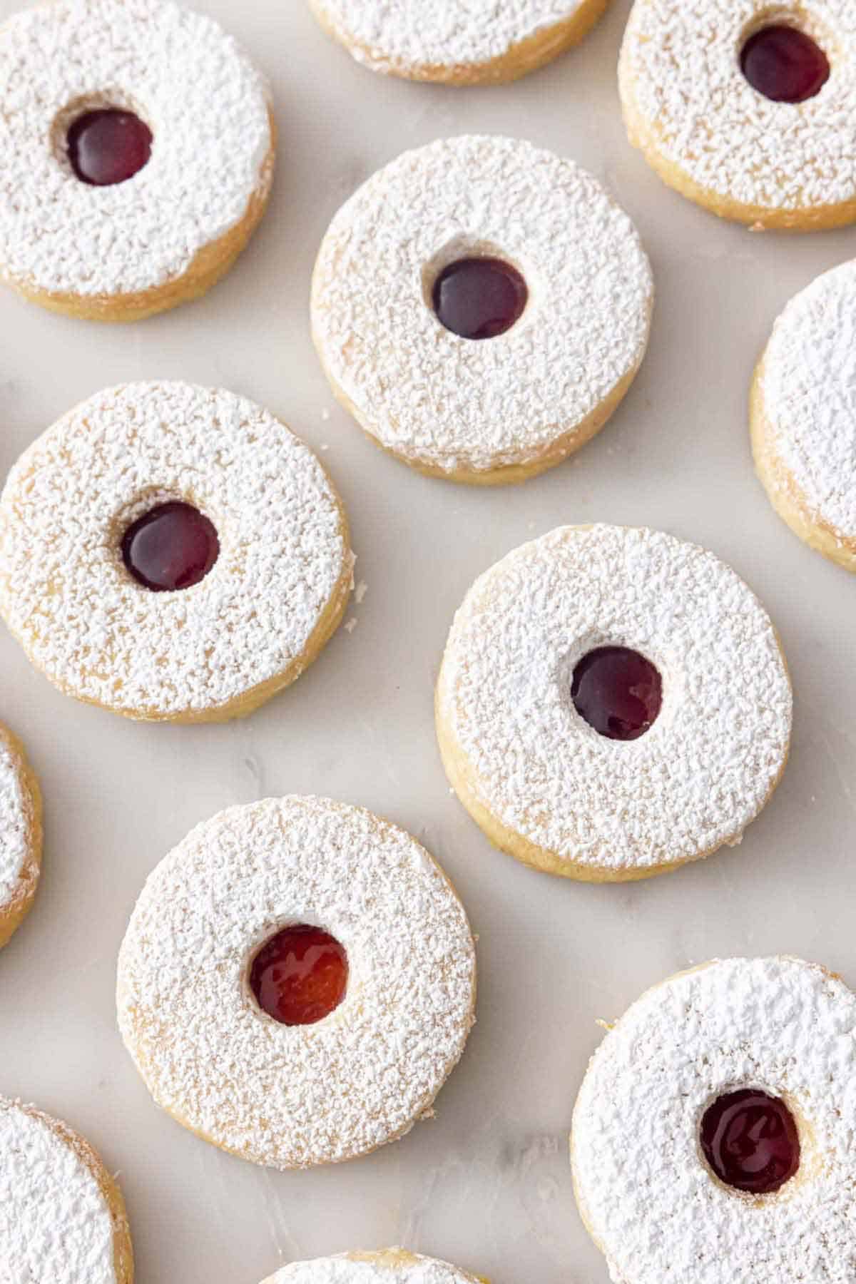 Multiple linzer cookies in a single layer on a marble surface.
