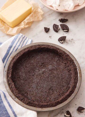 Overhead view of an Oreo pie crust in a pie pan and some Oreos, butter, and whipped topping in the background.