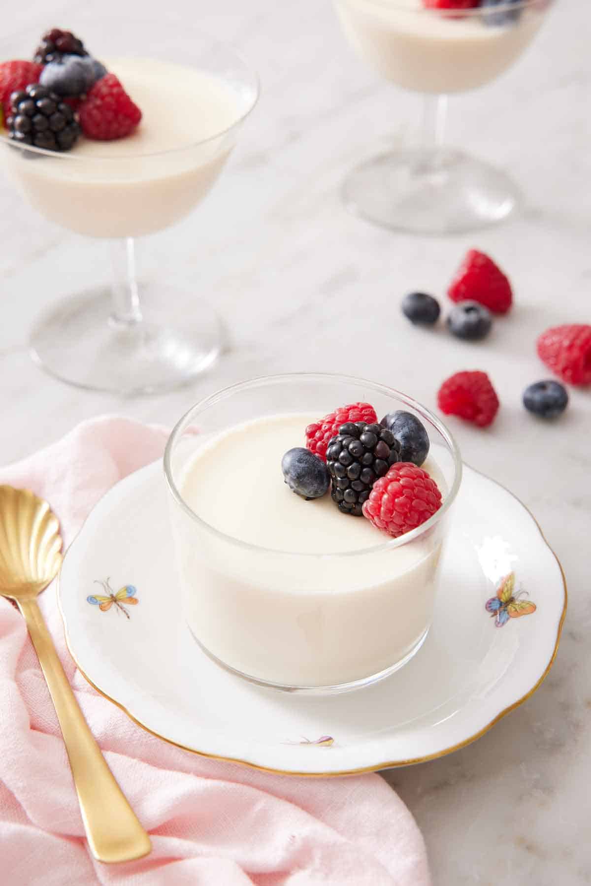 A plate with a glass of panna cotta topped with berries. More cups of panna cotta in the background.