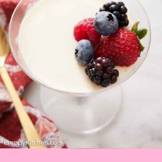 Pinterest graphic of a slightly overhead view of a glass of panna cotta with berries on top.
