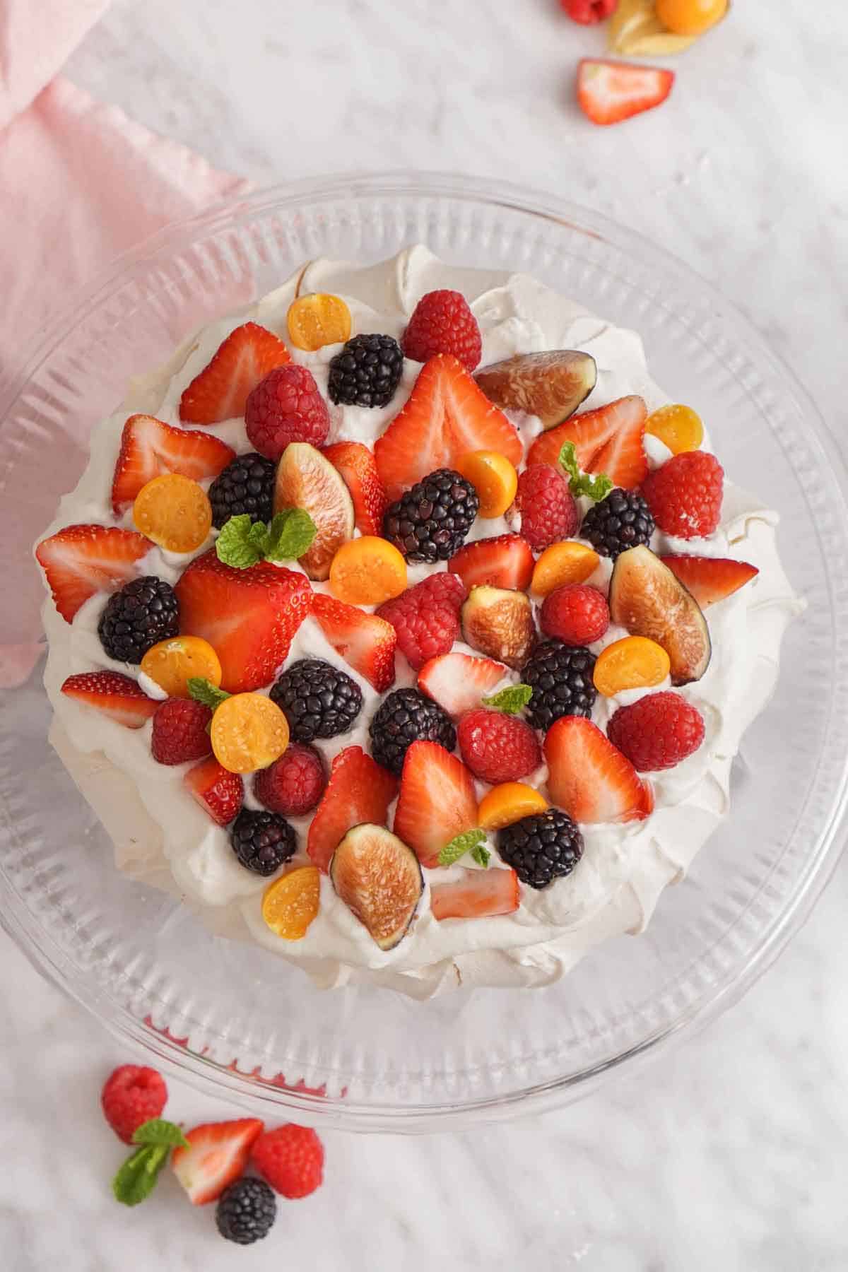 Overhead view of a pavlova on a cake stand with fresh berries on top.