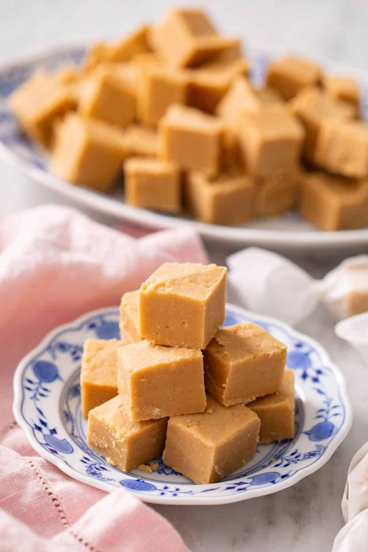 A plate with a pile of peanut butter fudge with a platter in the background.