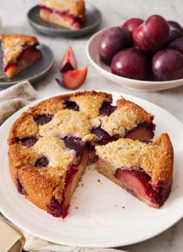 A platter with a cut plum cake with one slice cut and still on the platter.