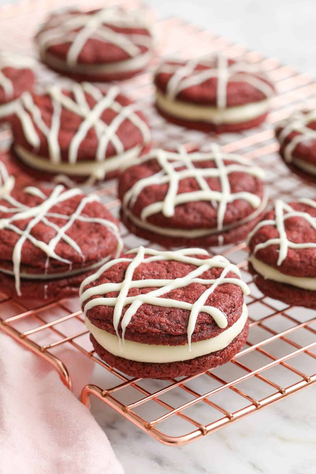 A cooling rack with red velvet cookies topped with drizzles of melted white chocolate.
