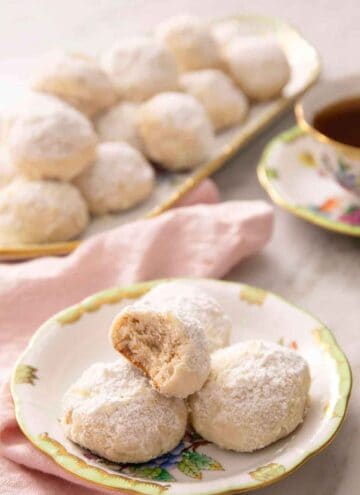 A plate with multiple Russian tea cakes with the one on top with a bite taken out of it. A platter more in the background.