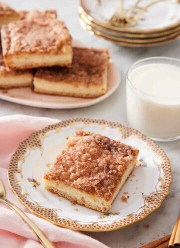 A square slice of a sopapilla cheesecake with a glass of milk and additional slices in the background.