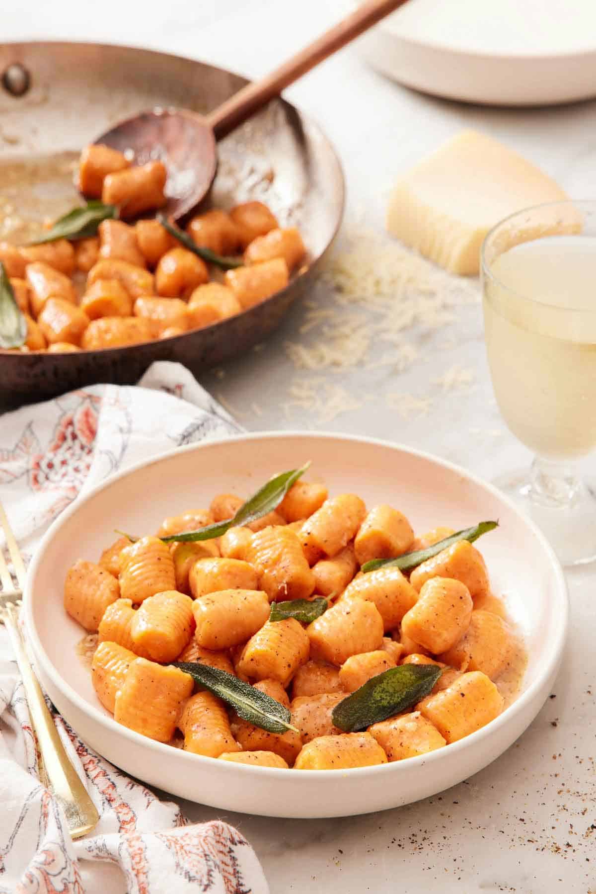 A plate of sweet potato gnocchi with sage leaves. A skillet of sweet potato gnocchi in the background.