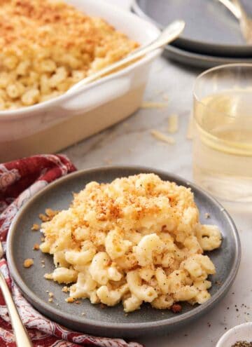 A plate with a serving of truffle mac and cheese with a baking dish and glass of wine in the background.