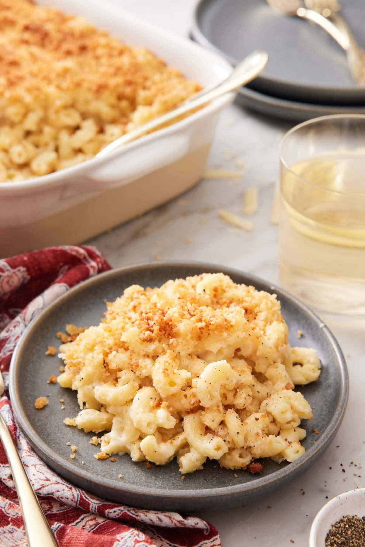 A plate with a serving of truffle mac and cheese with a baking dish and glass of wine in the background.