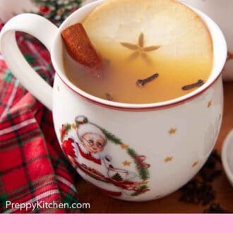 Pinterest graphic of a festive mug of wassail with a cinnamon stick, apple slice, and cloves.
