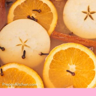 Pinterest graphic of close up view of wassail with cloves, cinnamon sticks, apple slices, and orange slices.