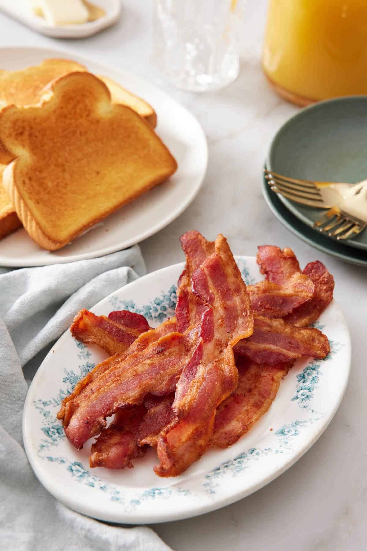 A platter of air fryer bacon with a plate of toast in the background along with a stack of plates and forks.