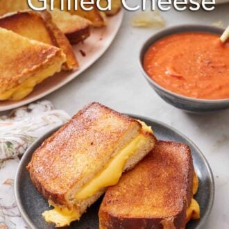 Pinterest graphic of an air fryer grilled cheese cut in half on a plate with more on a platter in the background along with a bowl of tomato soup.