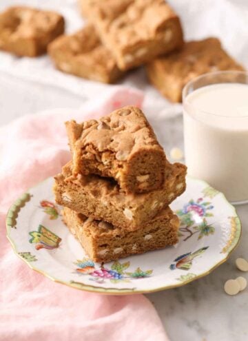 A stack of three blondies on a plate with a glass of milk in the back.