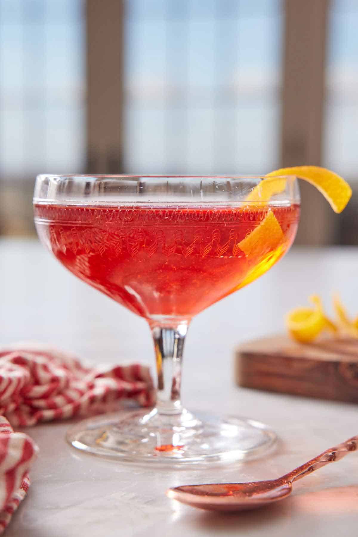 A glass of boulevardier with an orange twist garnish on the rim.