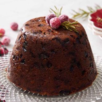 A platter with a Christmas pudding with sugared cranberries and rosemary on top.