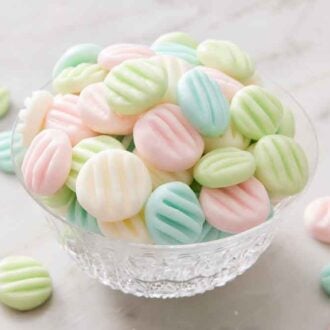 A bowl of cream cheese mints with more around it.