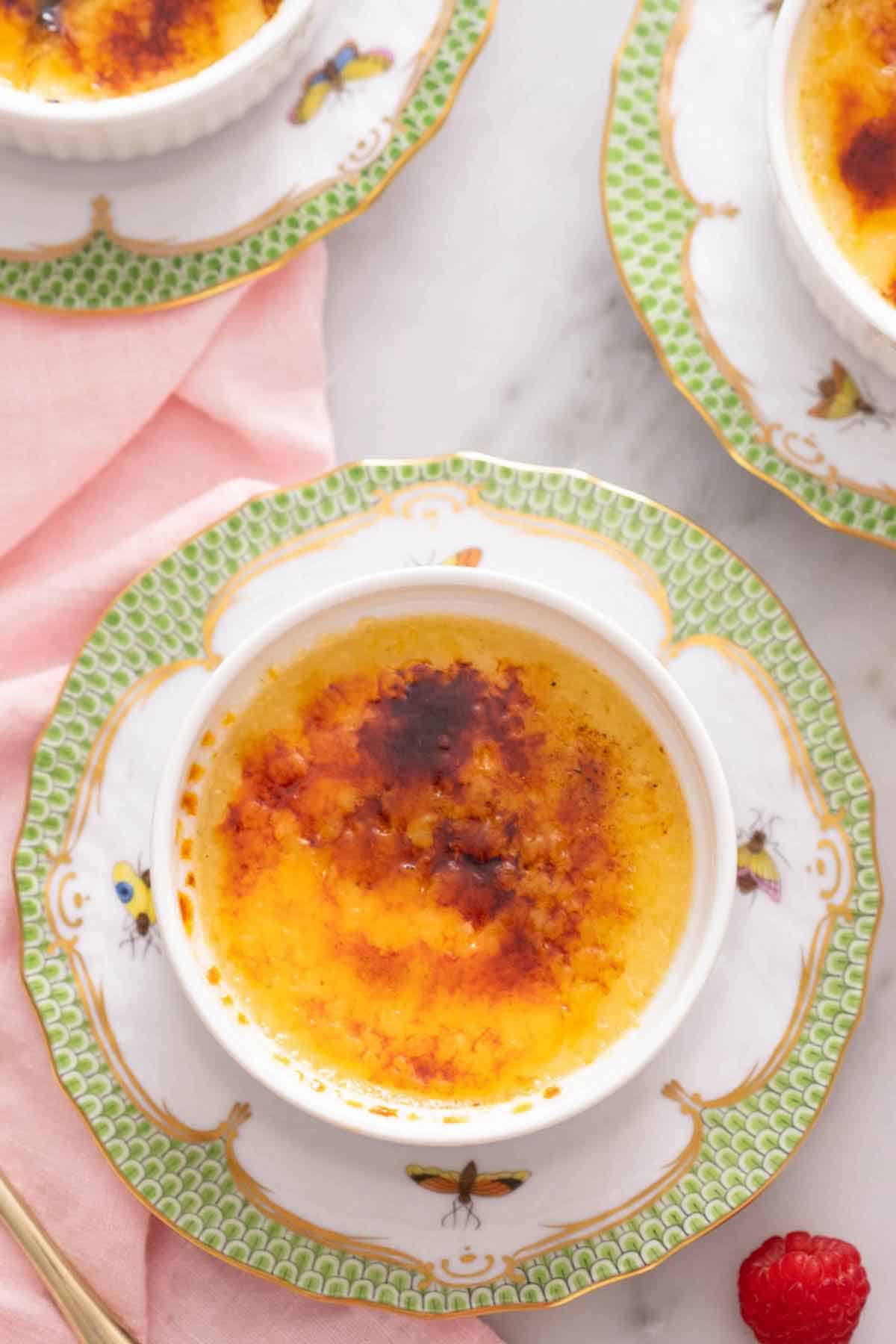 Overhead view of one of three crème brûlées on a serving plate with one in focus in the middle.